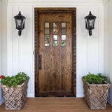 Wooden front door with decorative glass panels flanked by two outdoor lights and potted plants on a white wall.