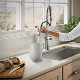 Person washing a white pitcher under a modern kitchen faucet with a scenic view outside.
