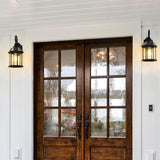 Wooden front door with glass panels flanked by two outdoor lights on a white wall.