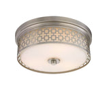 A brushed nickel finish flush mount lighting fixture with a laser cut shade and frosted white glass.